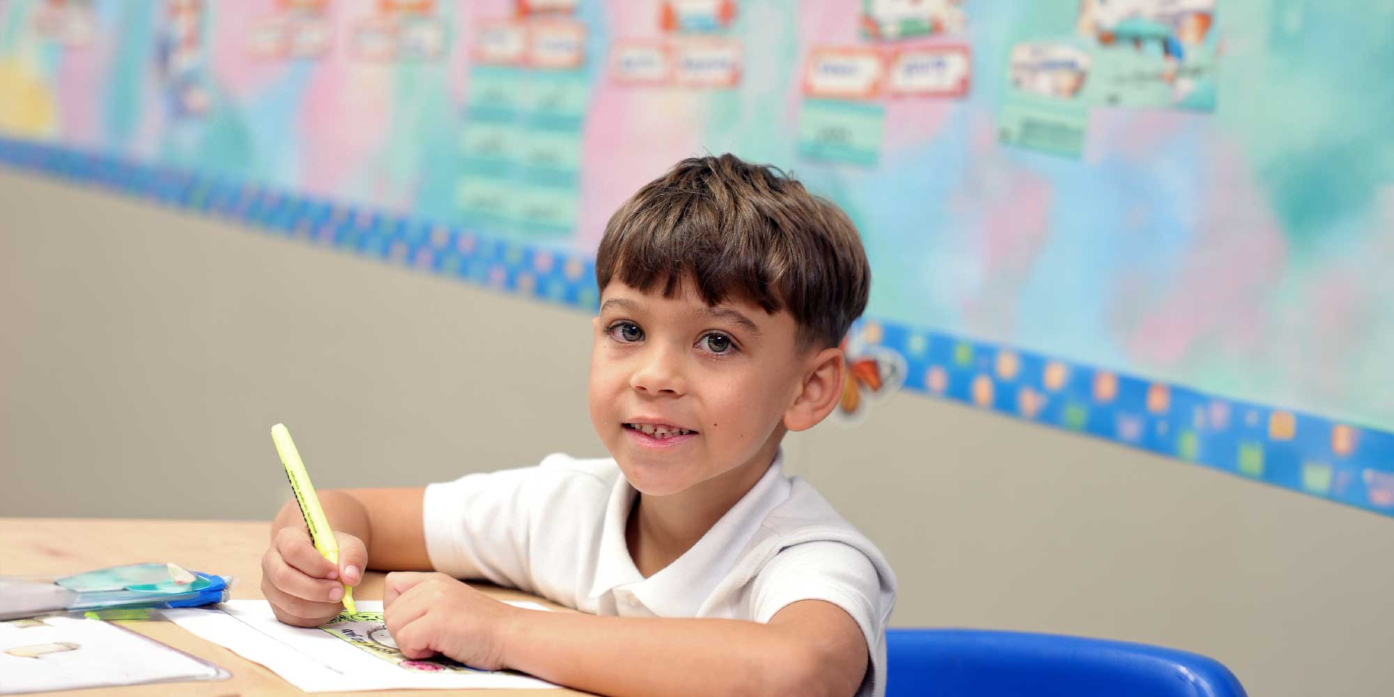 Young student coloring with a yellow marker at a classroom desk.