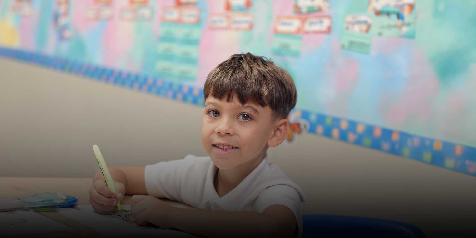Young student coloring with a yellow marker at a classroom desk.